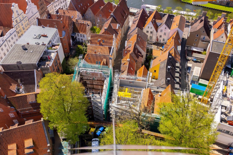Luftaufnahme einer Altstadt mit dicht gedrängten Häusern mit roten Ziegeldächern. In der Mitte des Bildes befindet sich eine Baustelle mit eingerüsteten Gebäuden und einem gelben Baukran. Grüne Bäume ragen zwischen den Häusern hervor.