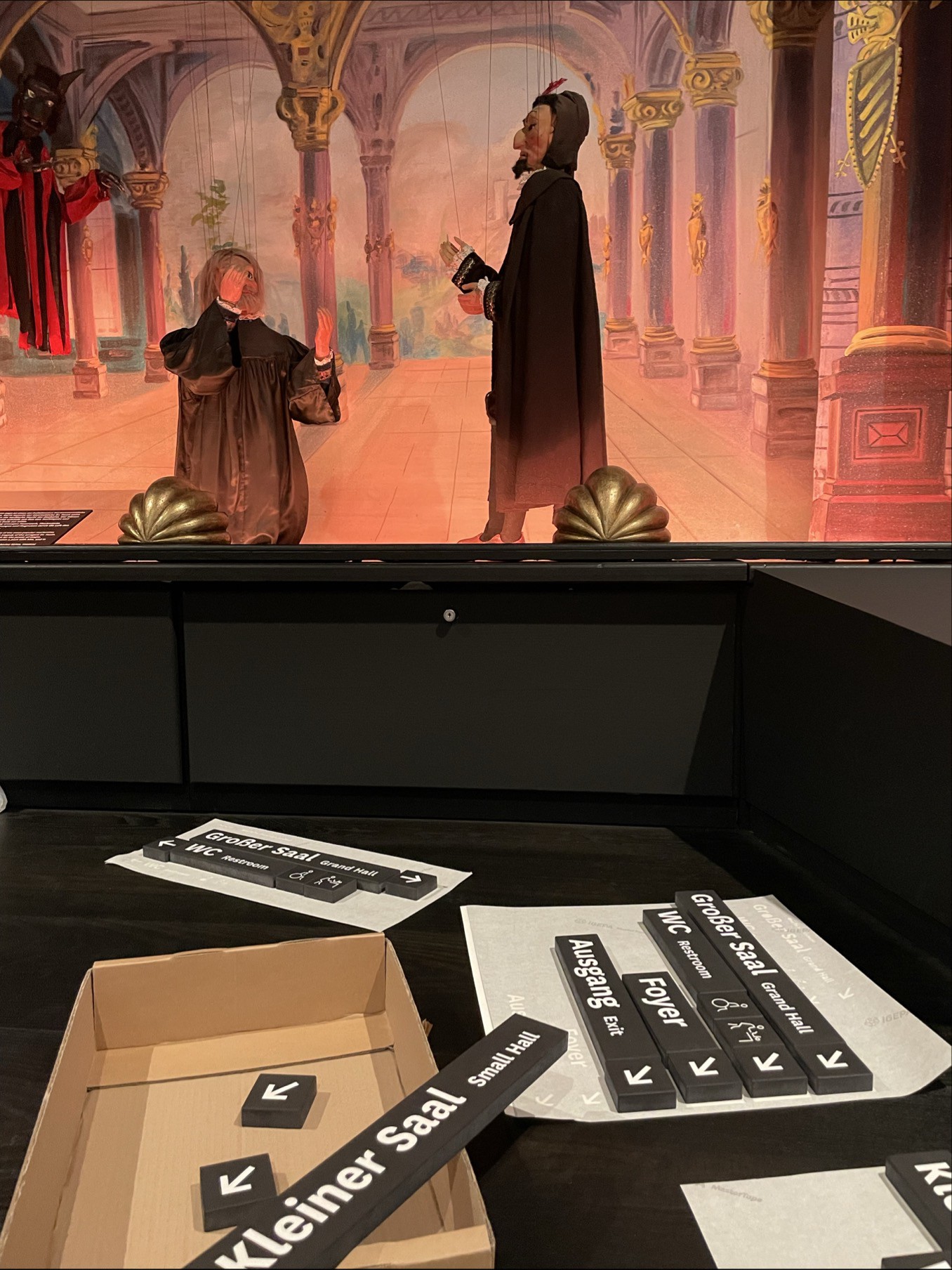 Beschilderung mit Figurenszene im Hintergrund